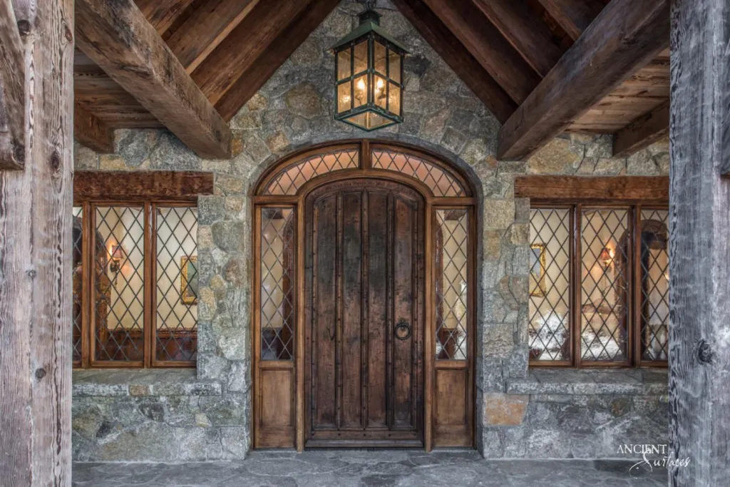Rustic stone entrance porch with a round arched wood door, iron lantern and heavy timber roof beams