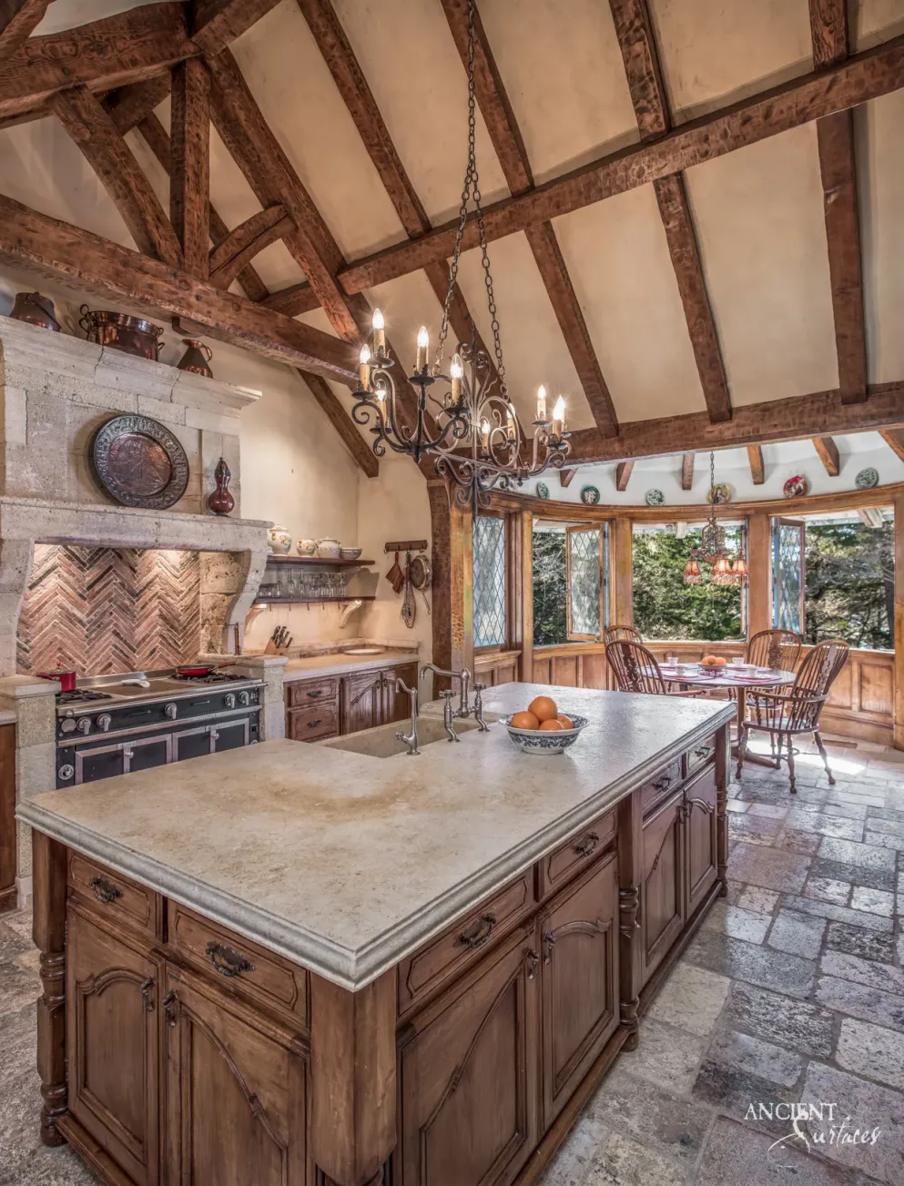 Carved limestone range hood and stone topped kitchen island in a beamed farmhouse kitchen