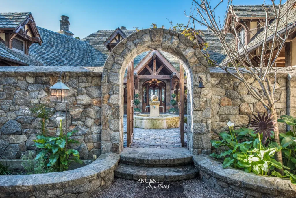 Rounded stone gateway arch framing a view of a courtyard fountain and covered timber porch beyond