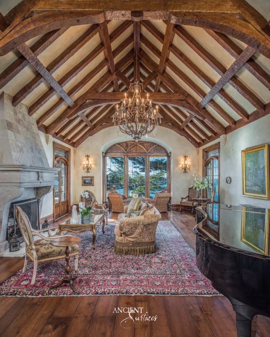 Carved limestone fireplace mantel beneath timber roof trusses in a coastal villa living room