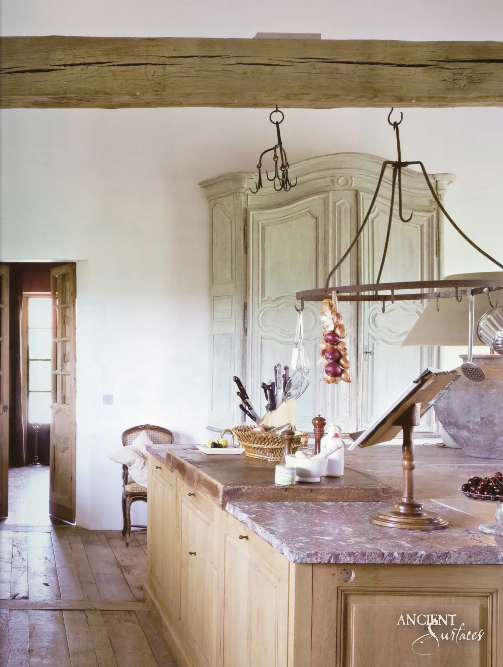 Weathered limestone countertop on a wood kitchen island standing before a painted antique armoire
