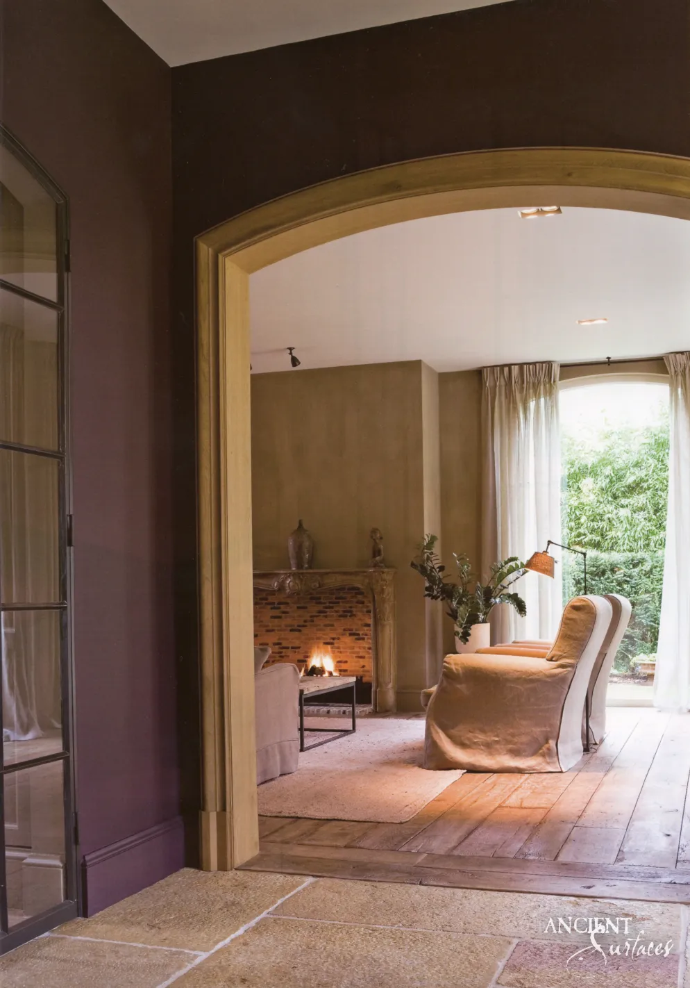 Antique limestone floor tiles at a rounded archway opening onto a living room with a lit fireplace