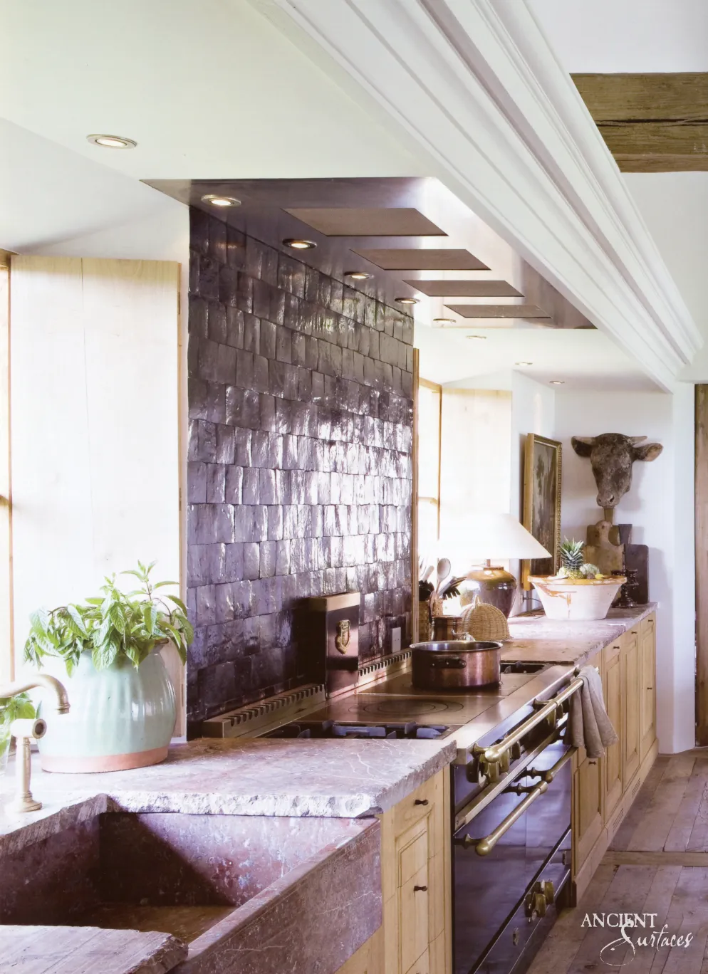 Mottled limestone kitchen countertop and integrated stone farmhouse sink beneath a dark glazed tile backsplash