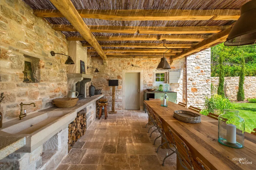 Stone hooded outdoor kitchen with a carved trough sink beneath a timber pergola