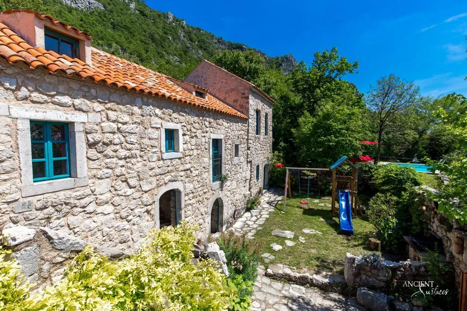 Rubble stone facade of a hillside villa with teal shuttered windows and a terracotta tile roof