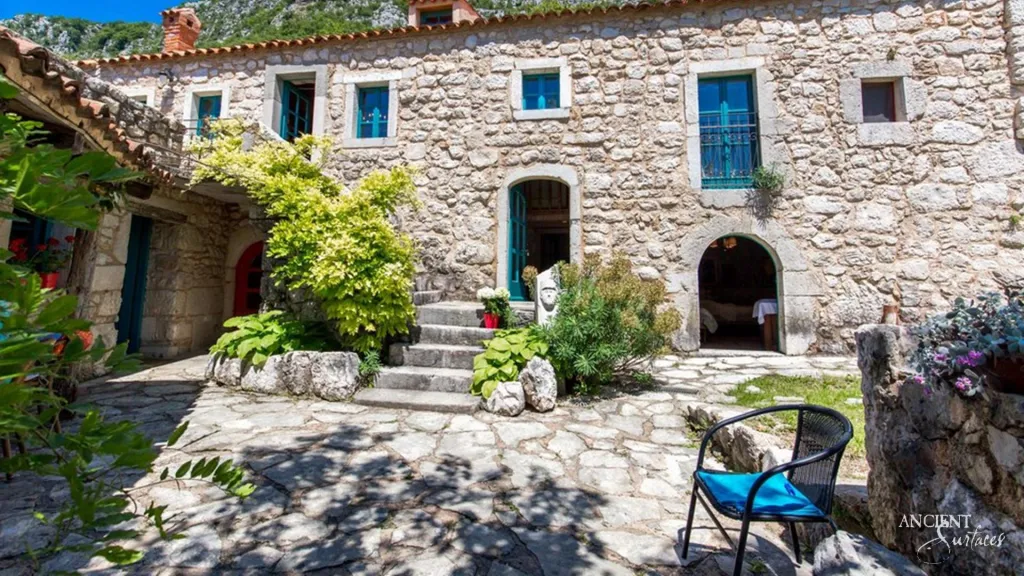 Front facade of a Croatian stone villa with an arched doorway, stone steps and teal shuttered windows